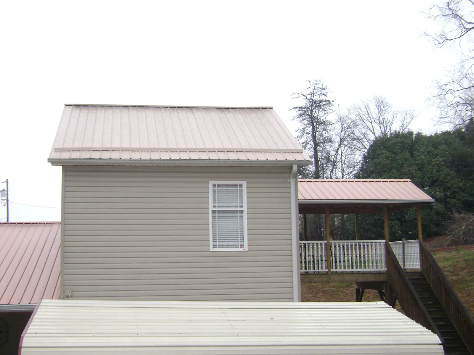 Tan metal roofs on a two story addition and attached porch, from a Roof Replacement job in Freedom